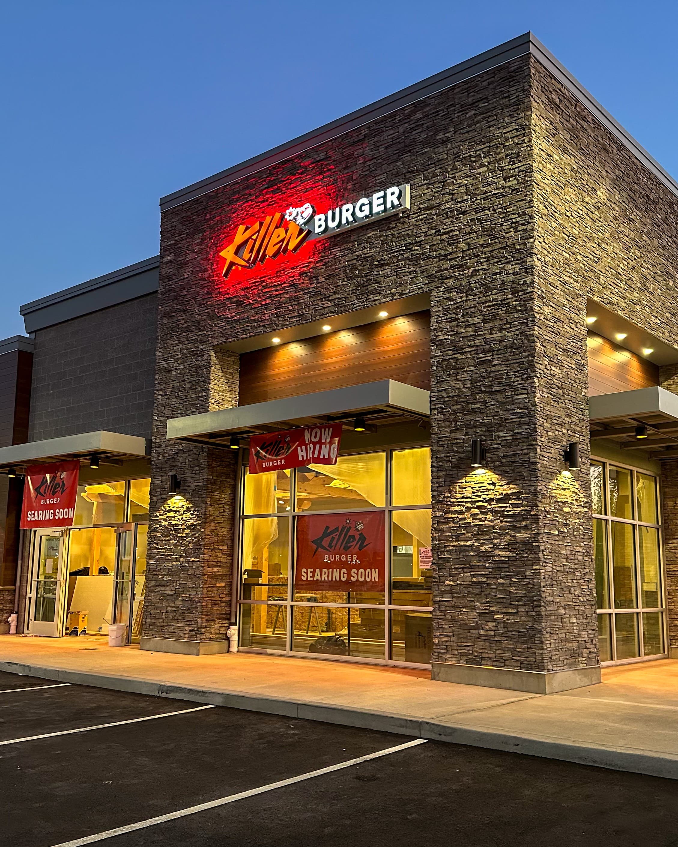 Killer Burger Bend — corner storefront exterior at dusk with illuminated signage and stone facade