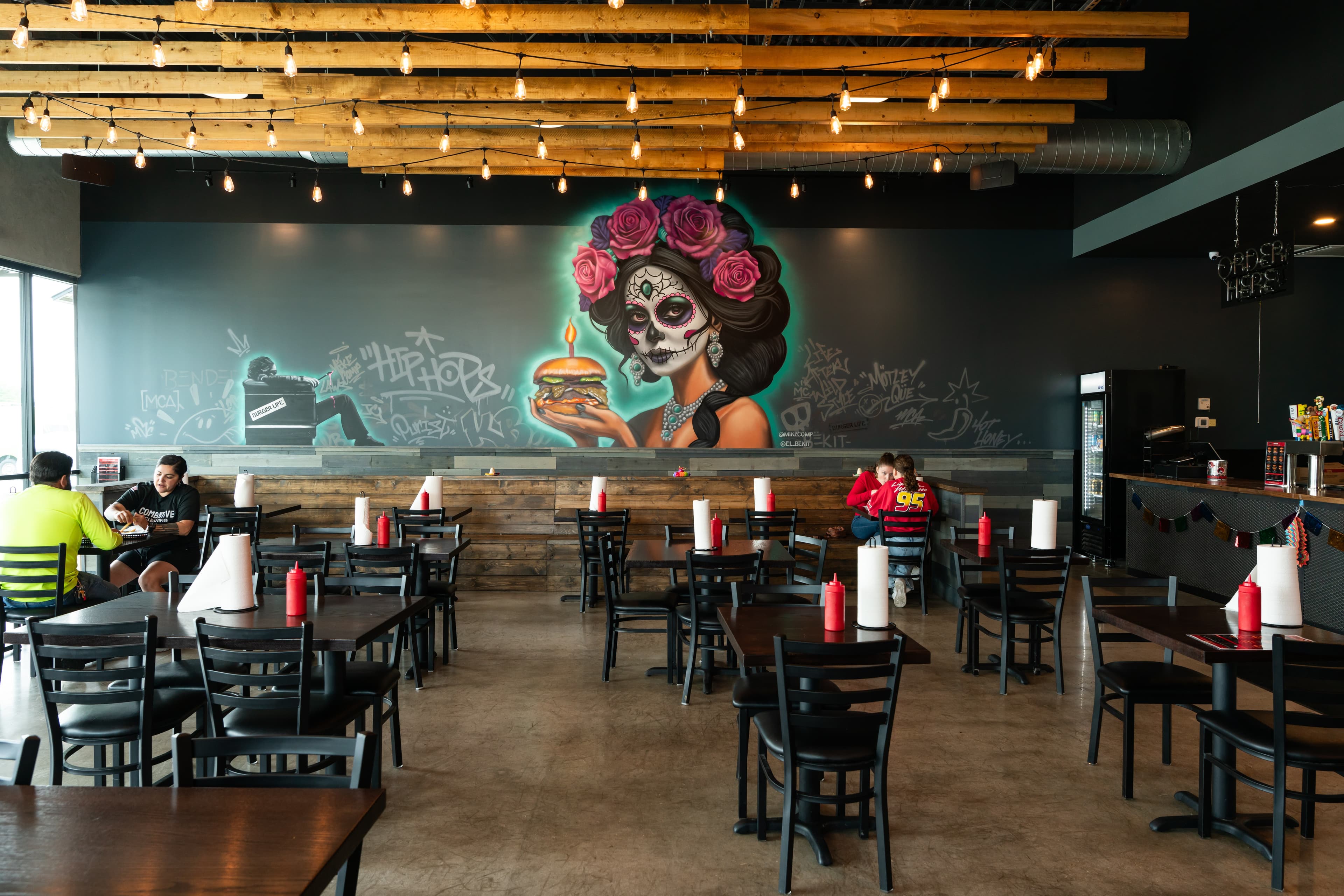 Killer Burger Potranco — interior dining room with Day of the Dead mural and string lights